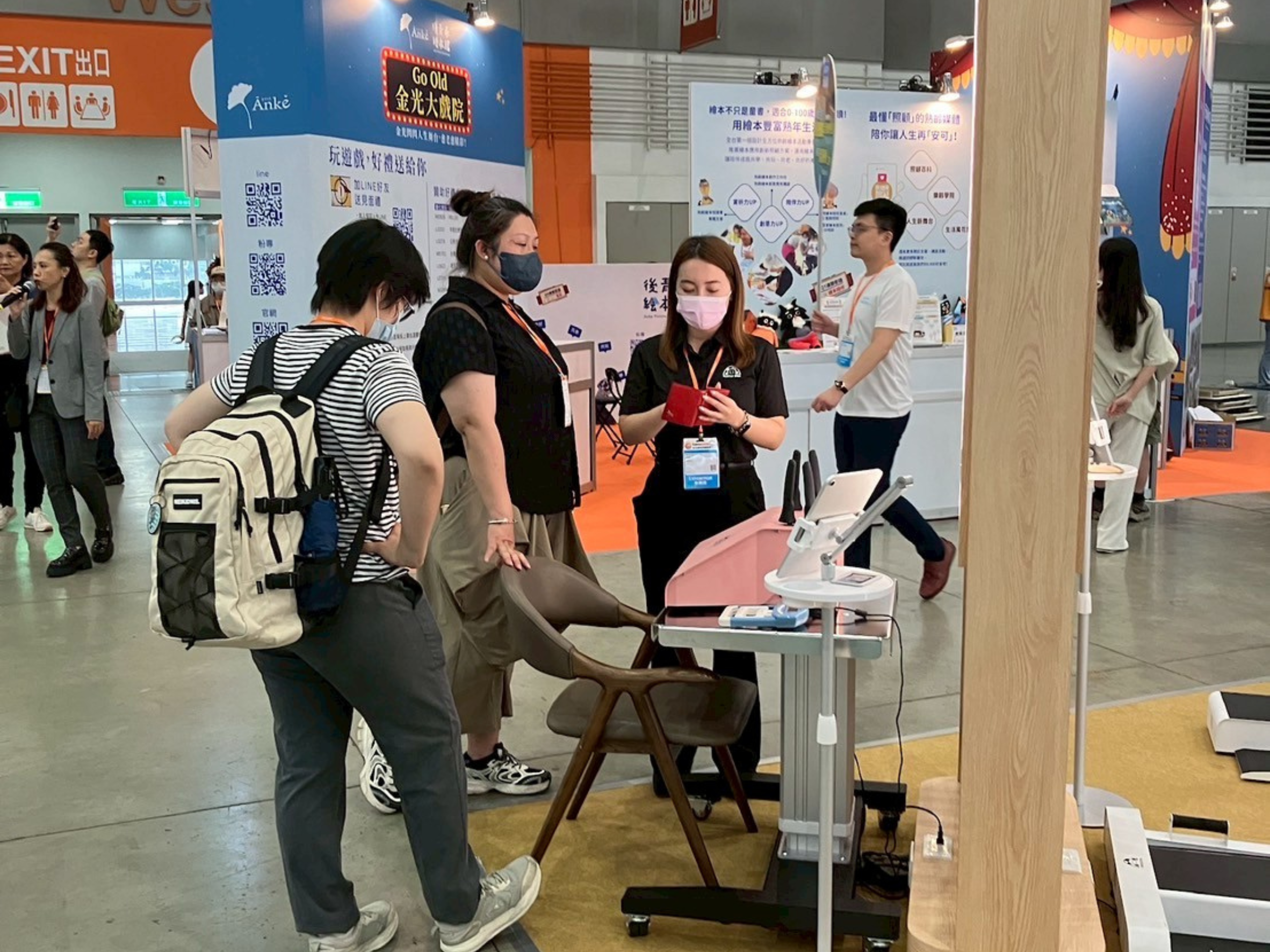 台北國際照顧博覽會展位實景。特多勁專業團隊正在向兩位參觀者介紹AI 智慧手部運動設備。