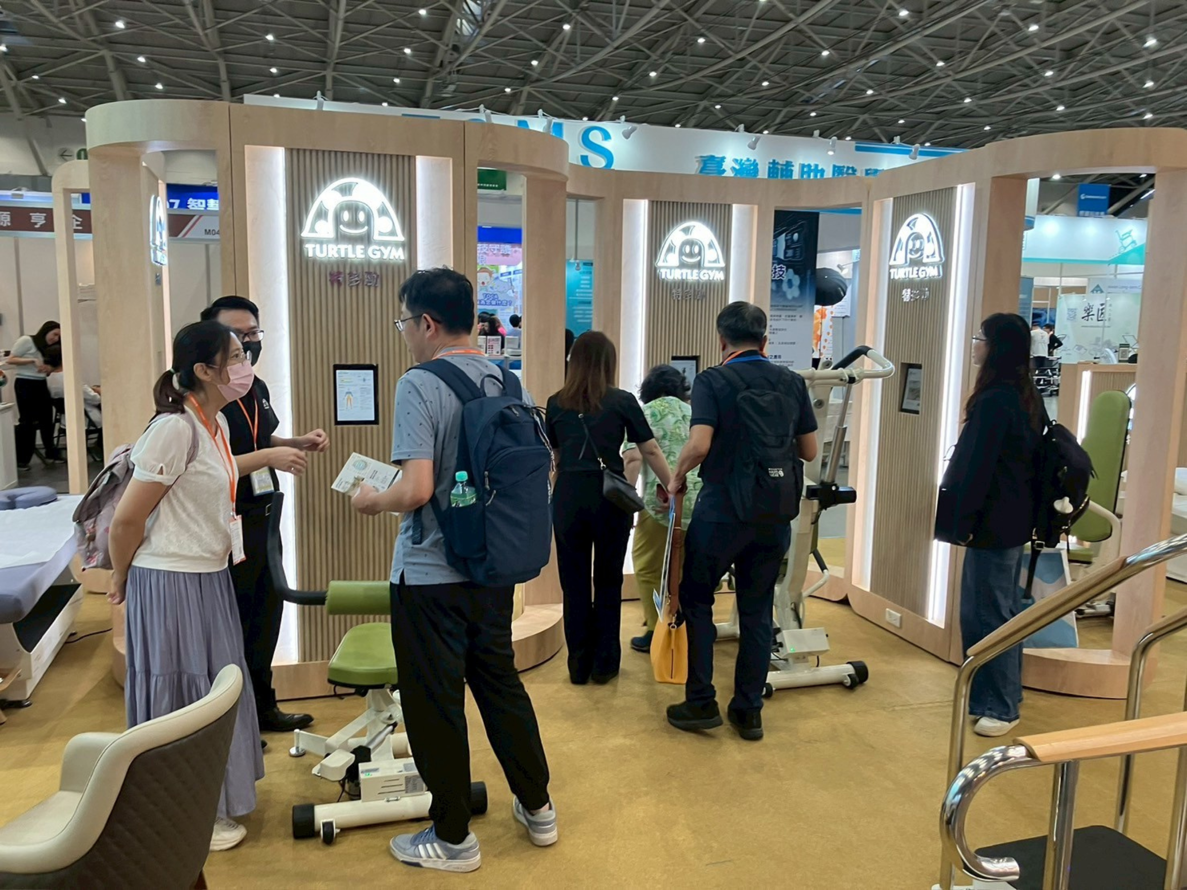 台北國際照顧博覽會特多勁展位，多位參觀者正在展位中與特多勁專業團隊交流，深入了解 AI 智慧銀髮運動解決方案。